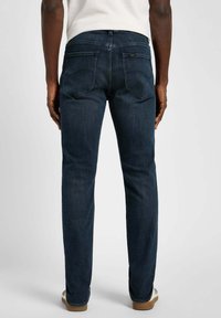 Jeans in denim scuro con una vestibilità slim, caratterizzati da tasche posteriori e una superficie liscia. Il punto vita presenta una piccola etichetta del marchio vicino alla parte posteriore.