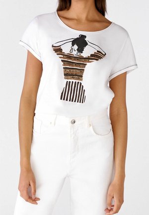 Biała bawełniana koszulka z okrągłym dekoltem, ozdobiona graficznym wzorem w brązowe i czarne paski, zestawiona z białymi jeansami.