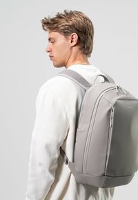 Grå ryggsäck med en slät, hållbar utsida, vadderade remmar och två dragkedjefack. Bärs på ryggen av en person.