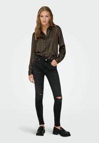 Blusa a rayas negras combinada con jeans skinny negros rasgados y mocasines negros. Tejido suave, diseño abotonado y silueta ajustada.