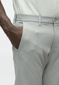 Gaiši pelēkas piegriezuma bikses ar gludu tekstūru, kas aprīkotas ar sānu kabatu, jostas cilpām un vienu pogas aizdari.