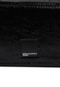 Błyszcząca czarna skórzana tkanina z małą czarną metalową płytką, na której wytłoczono białe litery "KARL LAGERFELD JEANS".