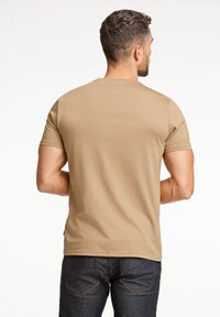 Beżowa koszulka z krótkim rękawem z miękkiego, gładkiego materiału, z okrągłym dekoltem i dopasowanym krojem, noszona z ciemnymi dżinsami.