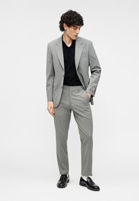 Γκρι κοστούμι με υφή, σακάκι μονόκουμπο, ταιριαστό παντελόνι, μαύρο πόλο μπλουζάκι από μέσα και μαύρα loafers.