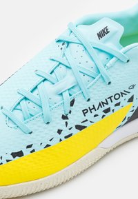 Buty Nike Phantom GT mają jasnoniebieską cholewkę o teksturowanej powierzchni, czarne akcenty, wyrazistą żółtą podeszwę oraz niebieskie sznurowadła.