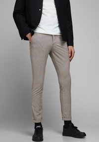 Beige mönstrade byxor med slim fit, tillverkade av ett mjukt tyg. Har uppvikta fållar och framfickor, tillsammans med svarta sneakers.