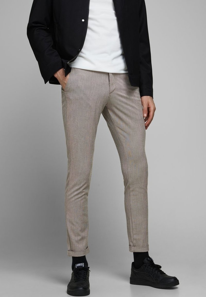 Beige mönstrade byxor med slim fit, tillverkade av ett mjukt tyg. Har uppvikta fållar och framfickor, tillsammans med svarta sneakers.