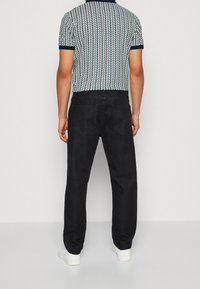 Jean en denim noir avec une coupe décontractée, associé à un polo en tricot texturé arborant un motif de feuilles bleu et blanc et des poignets contrastants.