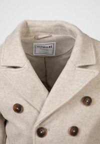 Bežist villasegu jope, millel on kahekordne rinnaesine, hammastatud krae ja neli pruuni nööpi. Sees on vooderdatud viimistlus.