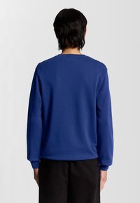 Blauwe sweatshirt met lange mouwen, ronde halslijn en geribbelde manchetten. Materiaal lijkt glad en zacht, met een effen kleur en geen zichtbare patronen.