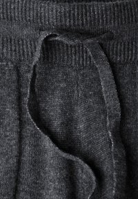 Pantalones de chándal de punto gris oscuro con una superficie texturizada. Presentan una cinturilla acanalada y un cordón a juego. Diseño suave y casual.