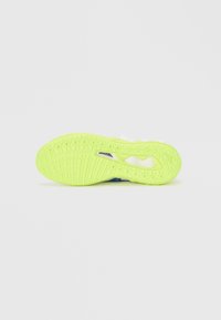 Σόλα λευκού και μπλε αθλητικού παπουτσιού με φωτεινή κίτρινο-πράσινη καουτσούκ επιφάνεια που διαθέτει κυκλικά και πλέγμα μοτίβα.