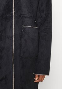 Cappotto blu scuro con una superficie morbida e testurizzata, caratterizzato da una tasca prominente, fodera chiara a contrasto e dettagli di cucitura visibili.