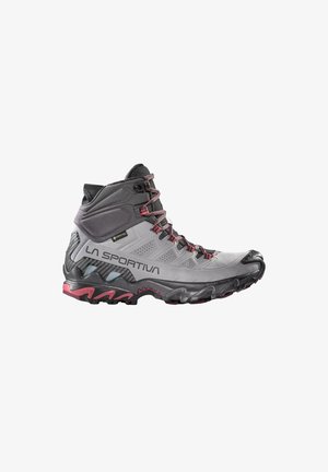 Grå og sort vandrestøvle med høj skaft og røde detaljer, forstærket tå og robust sål, mærket "La Sportiva" med Gore-Tex vandtæt label.