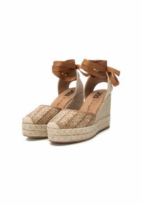 Sandalias de cuña con parte superior de yute beige trenzado, ataduras en los tobillos en tono marrón y plataforma envolvente de yute. Destalles de cuero suave y un tacón texturizado.