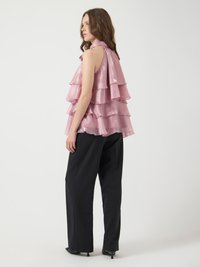 Rynkig rosa ärmlös topp med halterneck, lagerdesign och glänsande yta, ihop med svarta vida byxor och klackar.