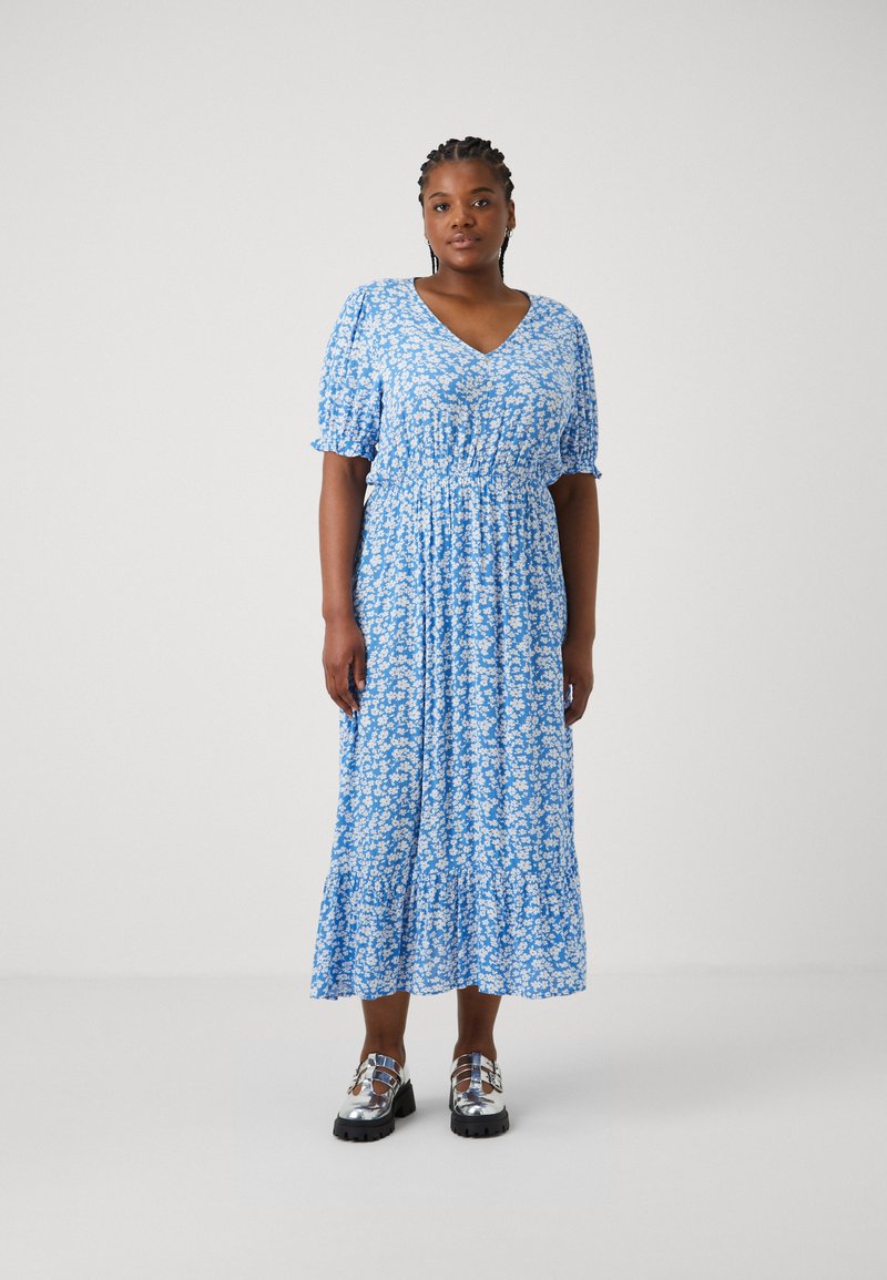 Μπλέ φόρεμα με λουλούδια, κοντά φουστανάκια, V-λαιμόκοψη και tiered φούστα. Συνδυασμένο με λαμπερά μαύρα παπούτσια πλατφόρμα.