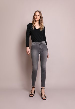 Top nero a maniche lunghe e jeans skinny grigi a vita alta. I jeans presentano una texture sbiadita e un leggero lavaggio, abbinati a tacchi neri con cinturini.