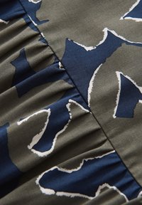 Gros plan sur un tissu avec un imprimé abstrait bleu marine et vert olive, des contours blancs et des plis froncés le long d'une couture.