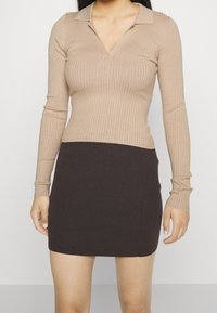 Beige geripptes Langarmoberteil mit V-Ausschnitt und brauem gerippten Minirock. Das Outfit hat ein tailliertes Design mit unterschiedlichen Texturen.