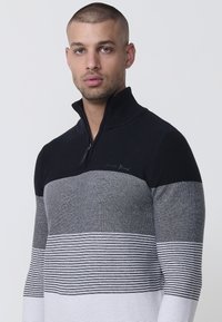 Schwarzer und grauer Zip-Pullover mit gestreiftem Muster, ausgestattet mit einem gerippten Muster und einem Logodetail auf der Brust.