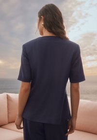 Haut à manches courtes bleu marine en tissu lisse, présentant une coupe droite et une discrète couture au dos, porté avec un bas assorti.