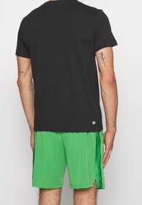 Black cotton t-shirt with short sleeves, paired with bright green mesh shorts featuring a side slit and "Ultra Dry" label on the back.