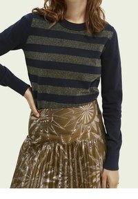 Jersey azul marino con patrón de rayas metálicas; cuello redondo y mangas largas combinado con una falda plisada en tono bronce con diseño de rayos de sol.