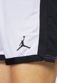 Pantalones cortos deportivos en blanco y negro con textura de malla. Presentan un estampado del logo de Jordan en negro cerca del dobladillo y una cinturilla sólida en negro.