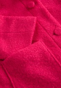 Lyserød uldfrakke med tekstureret overflade, reverskrave og store knapdetaljer. Inkluderer to påsyede lommer foran.