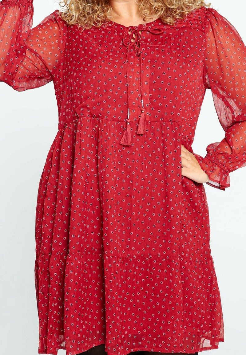 Robe rouge en tissu léger avec des motifs floraux. Elle présente un col rond, des détails à cordon de serrage et des manches puff transparents avec des poignets élastiques.