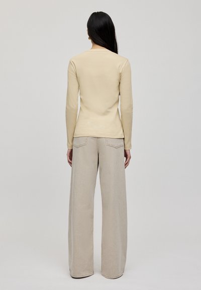 Langärmliges, figurbetontes beige Oberteil, kombiniert mit weiten beigefarbenen Hosen. Der Stoff wirkt glatt, mit einem schlichten Design und ohne sichtbare Muster.