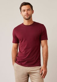 Burgundin värinen crewneck T-paita, joka on valmistettu puuvillasta, lyhyillä hihoilla ja vartalonmyötäisellä muotoilulla, yhdistettynä beigeihin housuihin.