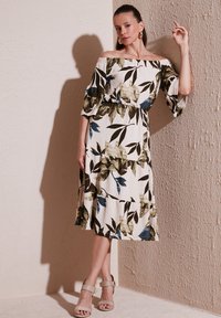 Off-the-shoulder, floral-printed dress with short puff sleeves, featuring a fitted waist and a flared skirt in beige, green, and blue tones.