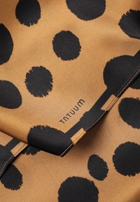 Brown fabric with irregular black polka dots, visible stitching, and the brand name "TATUUM" printed near the center.