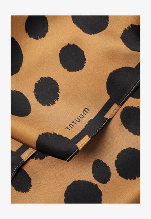 Brown fabric with irregular black polka dots, visible stitching, and the brand name "TATUUM" printed near the center.