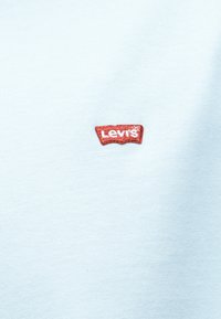 Ανοιχτό μπλε ύφασμα με μικρό κόκκινο σήμα Levi's κεντημένο κοντά στο κέντρο.