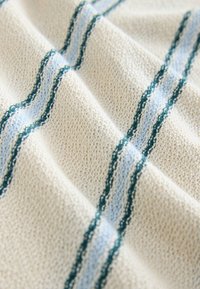 Textile featuring a cream base with textured surface; blue and green wavy stripes create a pattern. Soft and knitted appearance.
