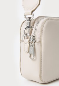 Kleine cremefarbene Handtasche aus glattem Leder mit silberner Hardware, ausgestattet mit einem oberen Reißverschluss und einer strukturierten rechteckigen Form.