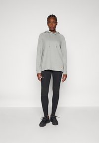 Grå hoodie med dragsko, lång ärm och en liten logotyp. Svarta leggings med texturerade knädetaljer. Svarta sportskor.