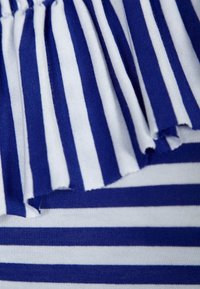 Modrá a bílá pruhovaná látka s plisovaným okrajem. Jemná, bavlněná struktura s střídavými širokými a úzkými pruhy.