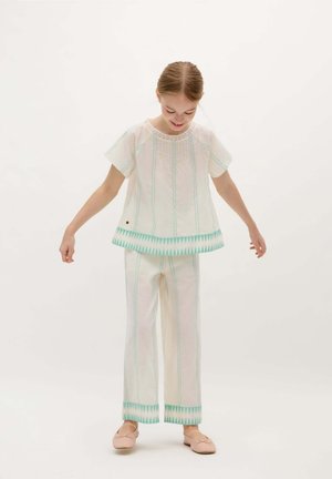 Conjunto de dos piezas que incluye una blusa blanca de manga corta con detalles en turquesa y bordados, combinada con pantalones blancos a juego, también con acentos en turquesa.