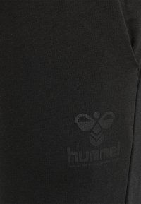 Svarta träningsleggings i ribbat tyg har en subtil, ton-i-ton logotyp på vänster sida. Materialet har en slät, elastisk textur.