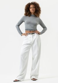 Grijze langslavende crop top gecombineerd met witte high-waisted wijde broek. De broek heeft plooien en een zwarte riem met een gouden gesp.