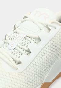 Close-up van een witte sportschoen met mesh ontwerp, witte veters, en "TYR" branding op de tong en "CXT-2" label op het vetergebied.