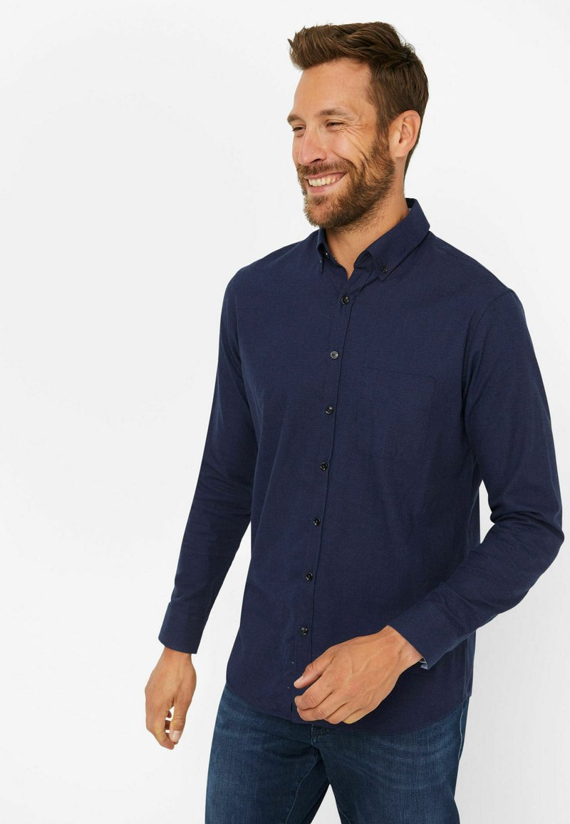 Marineblaues Langarmhemd aus strukturiertem Stoff, mit Button-Down-Kragen, Brusttasche und schwarzen Knöpfen. Getragen mit Jeans.