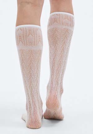 Chaussettes blanches en dentelle montant jusqu'au genou, avec des motifs complexes en forme de feuilles, une texture douce et des bords élastiques pour un maintien sûr. Matériau translucide.