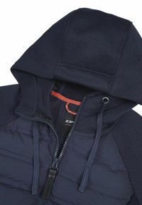 Marineblaue Kapuzenjacke mit Frontreißverschluss, verstellbaren Kordeln und gepolstertem Brustbereich, zeigt Innenlabel und roten Aufhänge-Ring.