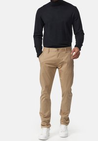 Beige chinos met een slim fit, voorzien van zijzakken, riemlussen en een knoopsluiting, gecombineerd met een zwart overhemd met lange mouwen en witte sneakers.