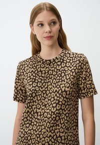 Bruine t-shirt met een luipaardprint in beige. Korte mouwen en een ronde halslijn. Zachte textuur, casual ontwerp.